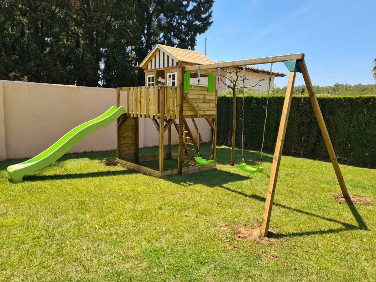 Parc infantil format per una caseta Lollipop XL posada a una plataforma amb escala, paret d'escalada i rampa de tobogan. Aquesta versió a més a més té un gronxador.